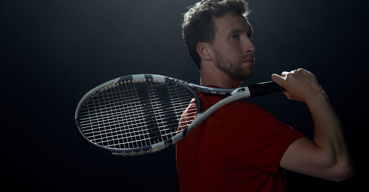Portrait of a male athlete with a tennis racket in a dark studio setting, highlighting his profile.