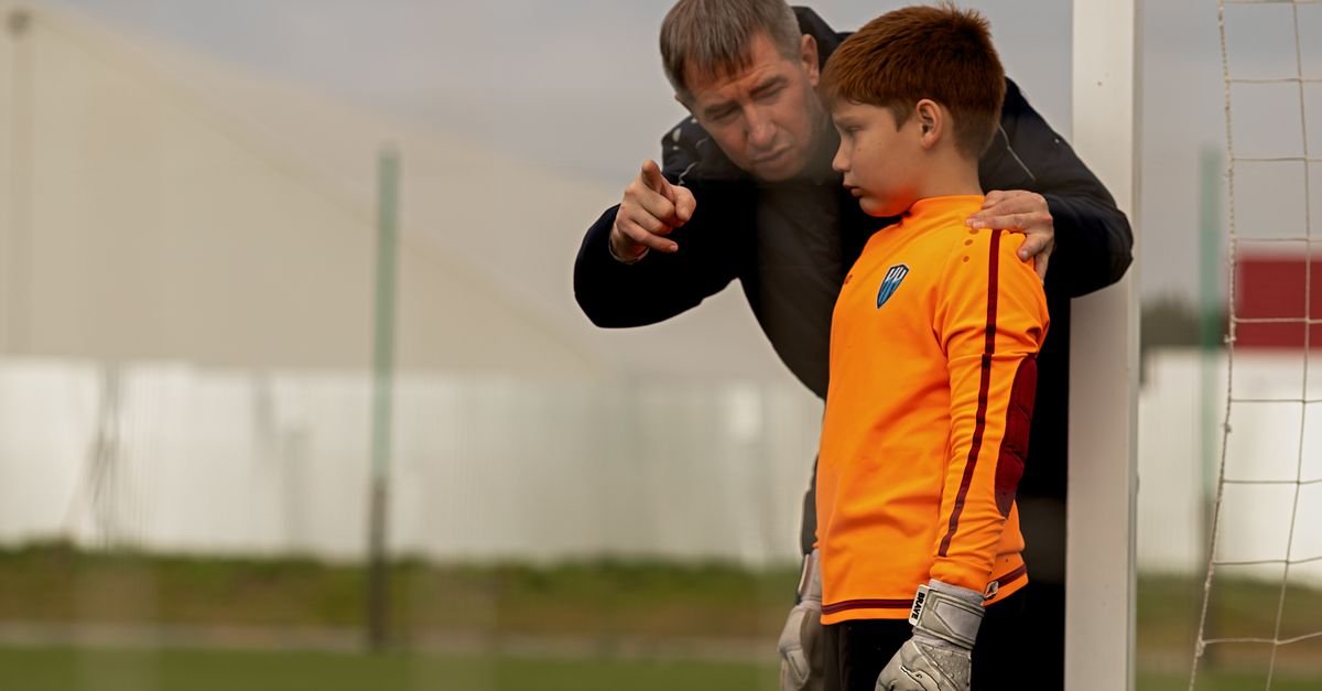 A coach providing guidance to a young goalkeeper on a soccer field.