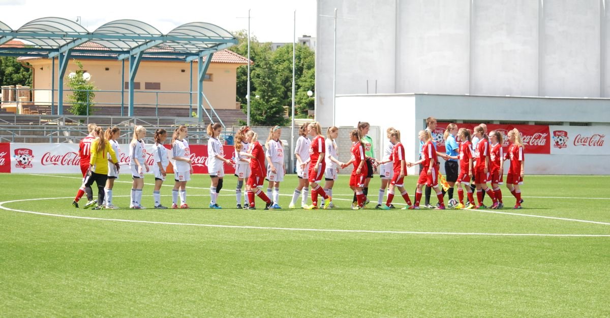 Young women's soccer teams in uniforms shaking hands on the field, promoting sportsmanship.