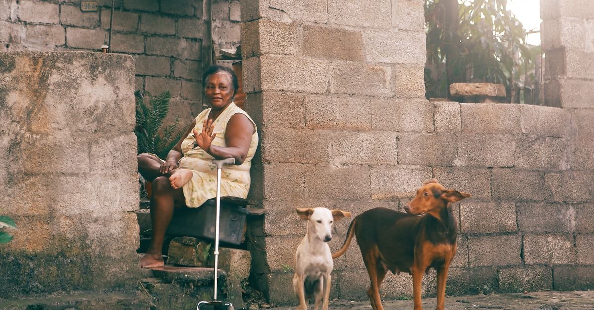 Senior woman sitting with her dogs outside her home in a rustic setting.