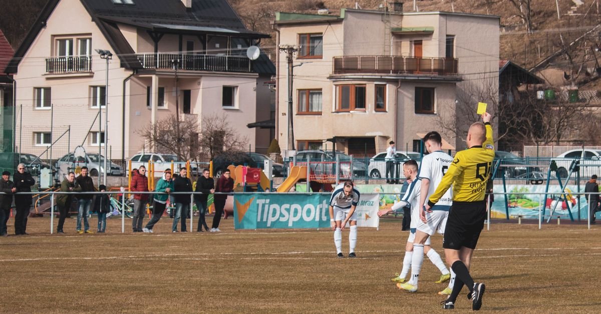A lively soccer match in Domaniža, Slovakia, showcasing a referee giving a yellow card.
