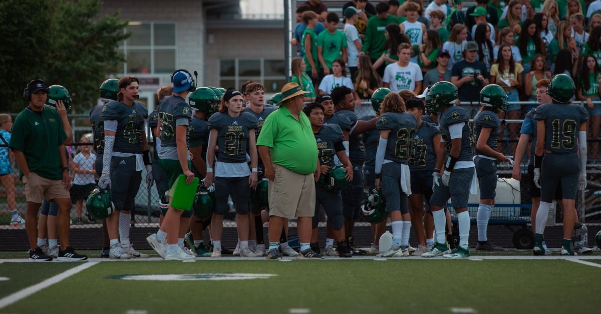 High school football players and coach on sidelines during a game.