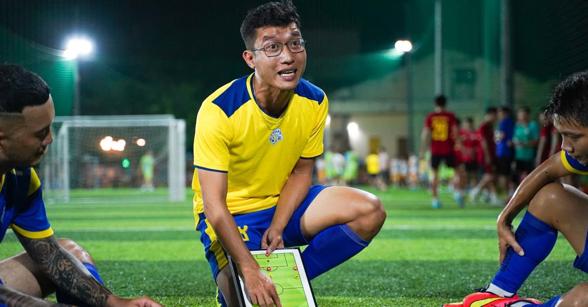 A soccer coach strategizing on a field with players during a night game session.