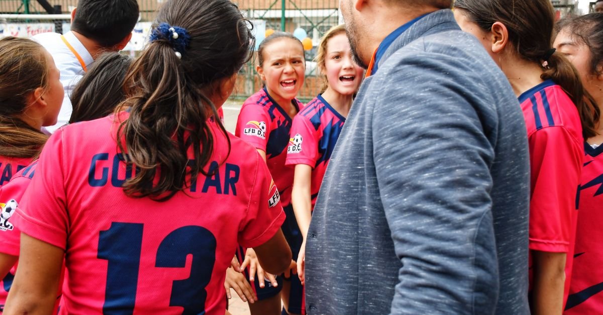 A vibrant moment capturing a youth soccer team in a motivational huddle with their coach, outdoors.