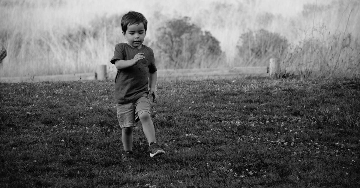 A young child joyfully running in a grassy field in monochrome.