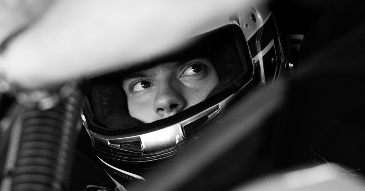 Black and white photo of a race car driver intensely focused, wearing a helmet.
