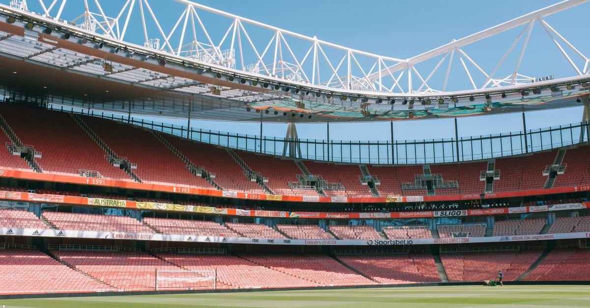 Wide view of Emirates Stadium's empty stands under a clear blue sky in London.