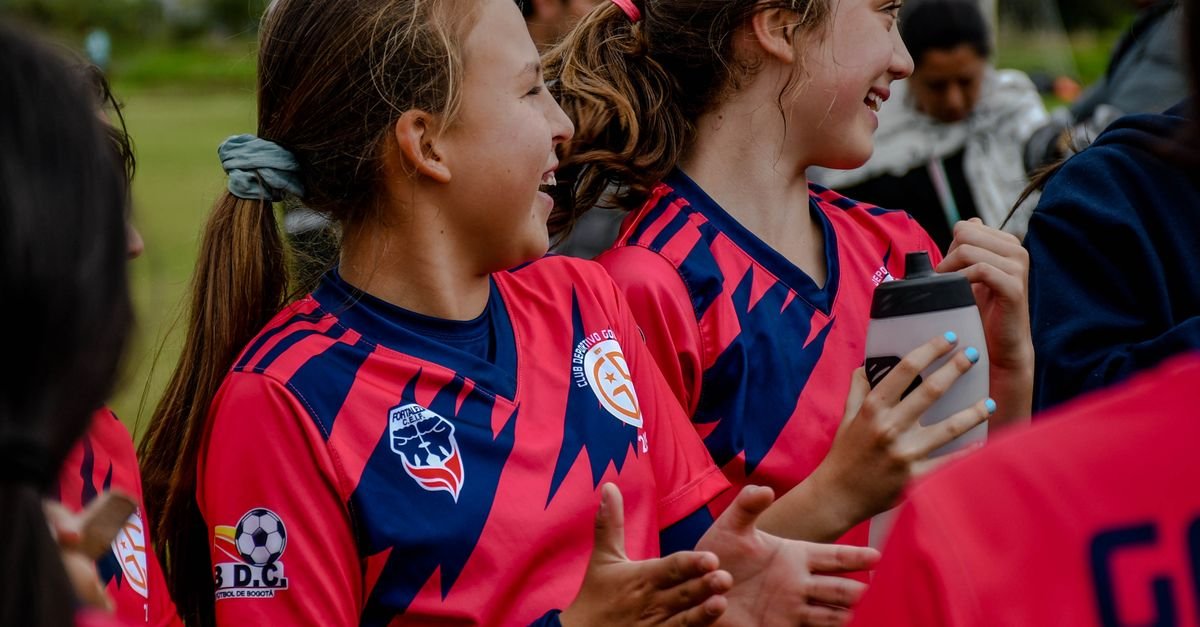 Happy young girls in sportswear celebrating a soccer match victory on an outdoor field.