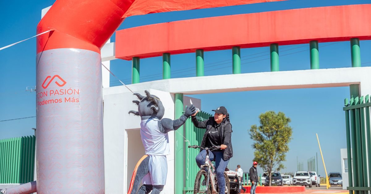 A cyclist receives a high-five from a mascot at the finish line of a cycling event under a clear blue sky.