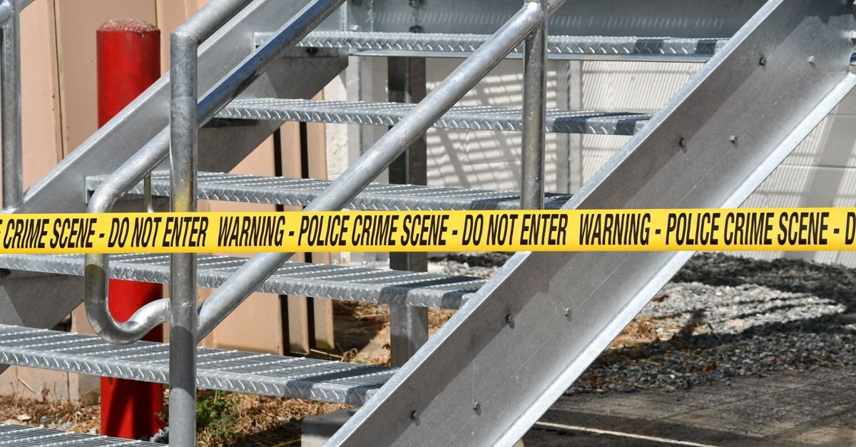 Close-up of a metal stairway blocked by yellow police crime scene tape outdoors.