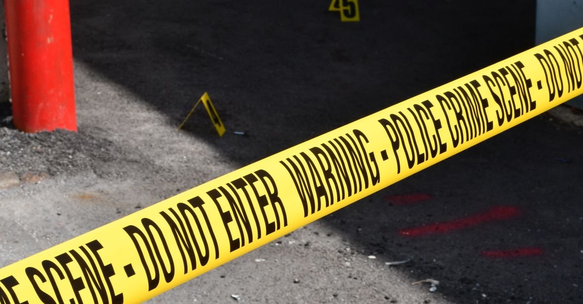Yellow police crime scene tape marking a restricted urban area on concrete ground.