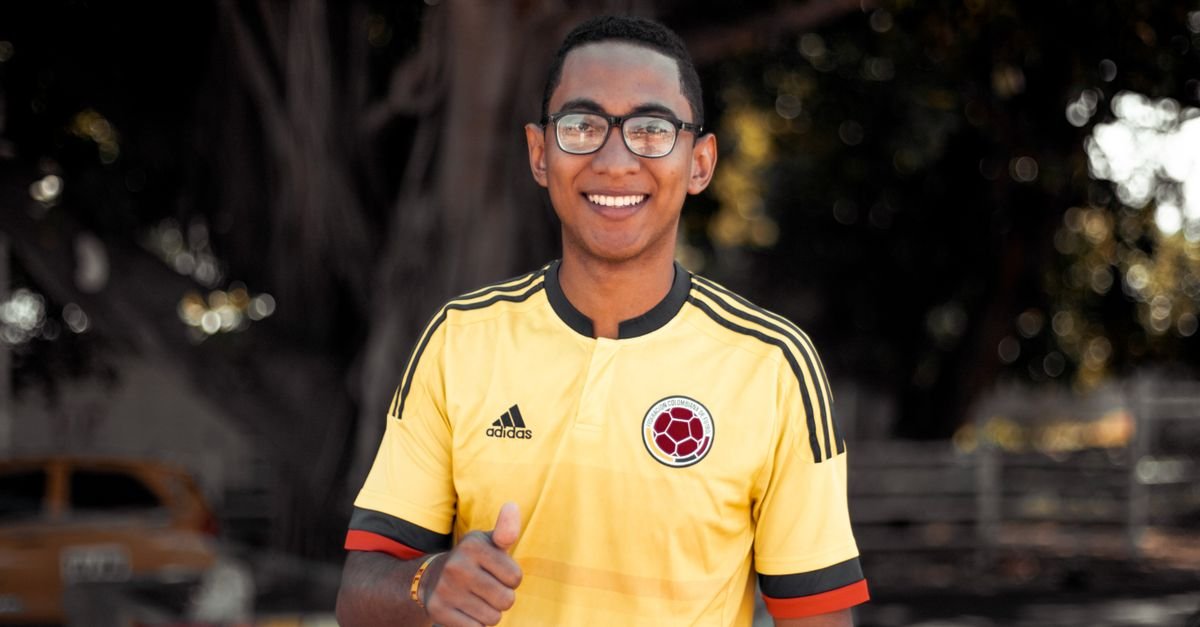 Smiling man wearing a sports jersey outdoors, giving a thumbs-up gesture.