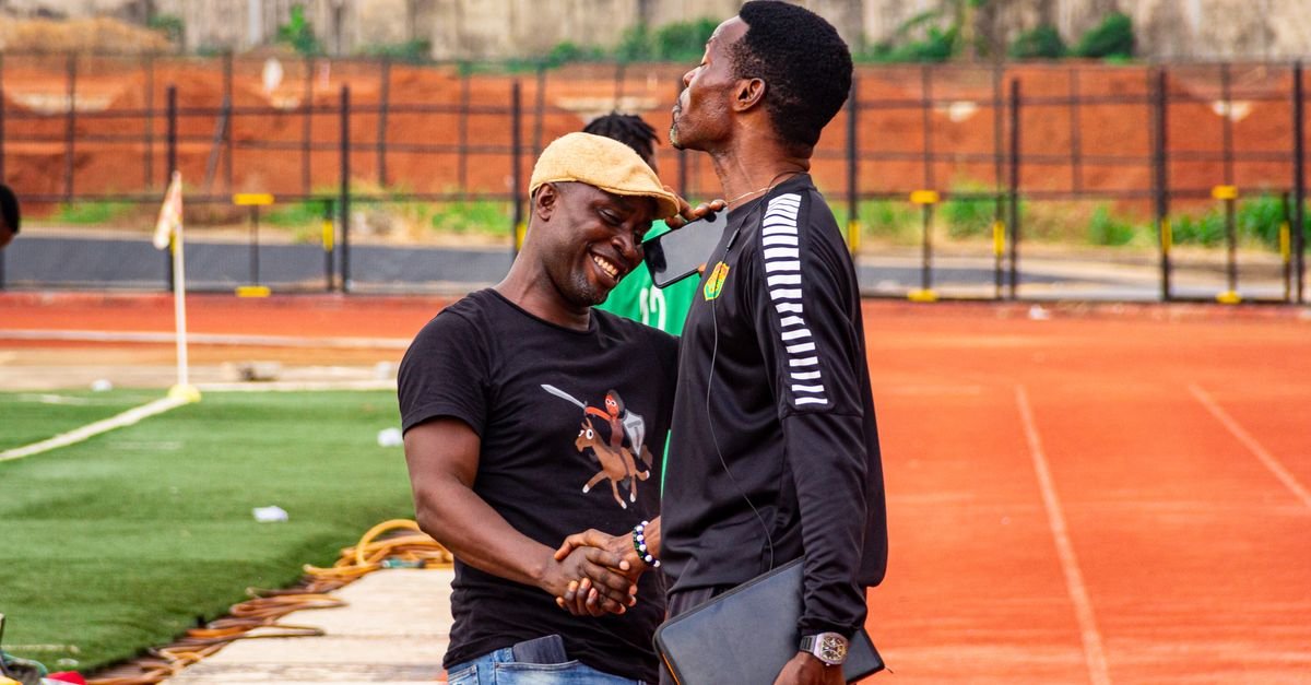 Two men share a joyful handshake on a soccer field, symbolizing friendship and sportsmanship.