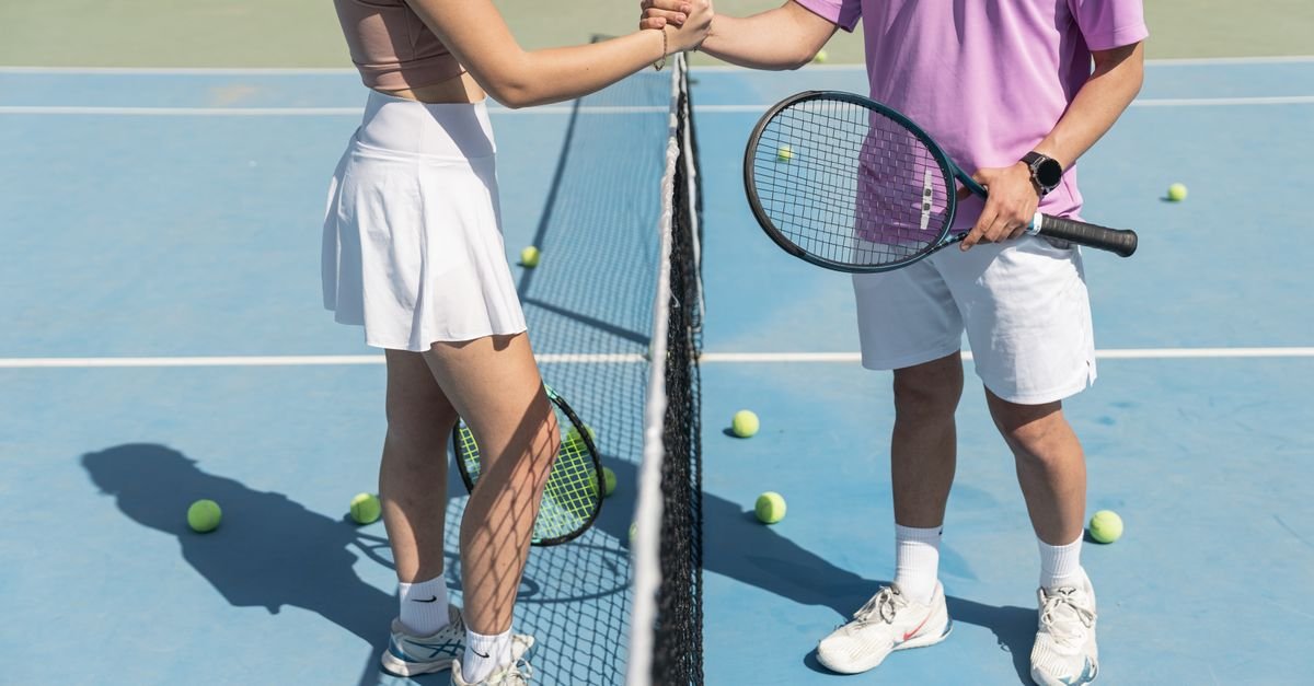 Two tennis players shaking hands over the net on a sunny day, symbolizing sportsmanship.