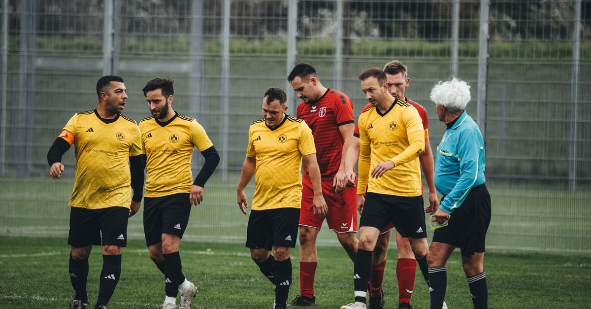 Amateur soccer players in yellow uniforms and referee on the field after a match.