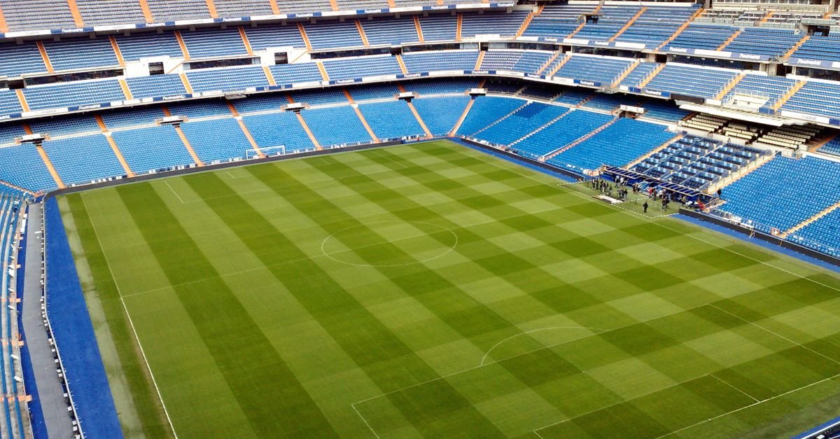 Aerial view of an empty soccer stadium with neatly trimmed green field and blue seating arrangements.
