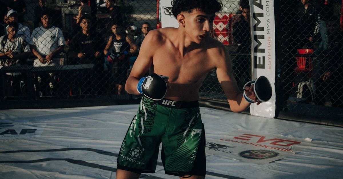 Young male fighter in action during an MMA fight in a cage.