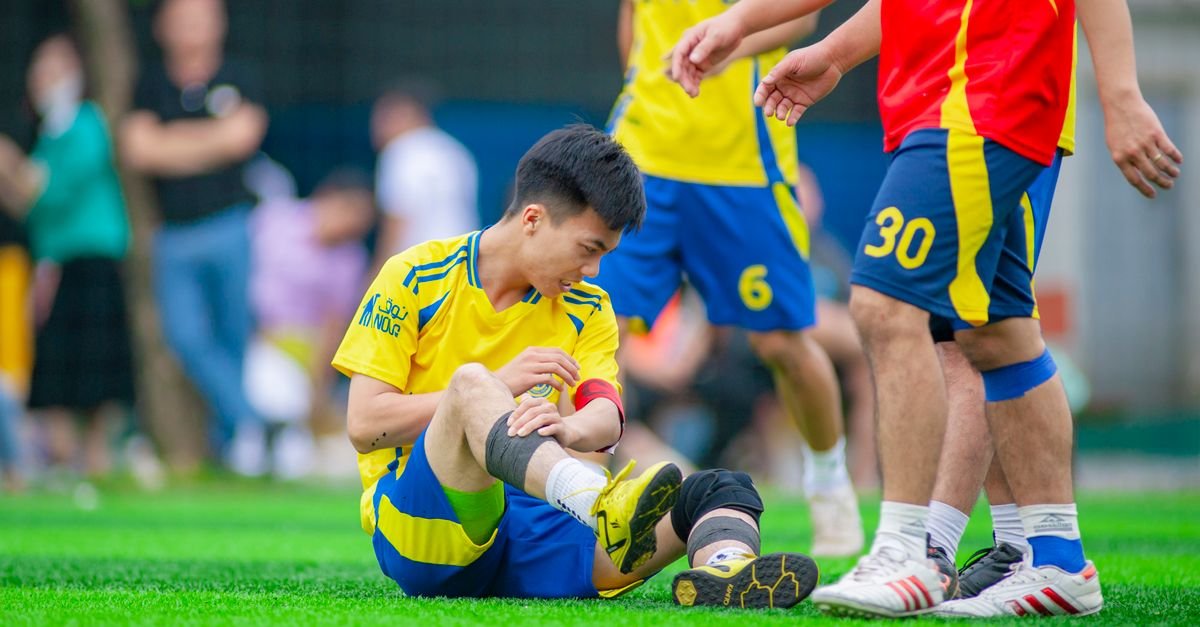Amateur soccer player sitting on grass, nursing a leg injury during game in Hanoi, Vietnam.