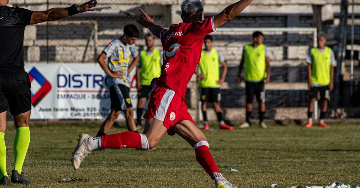 A soccer player in red celebrates a goal with enthusiasm on an outdoor field.