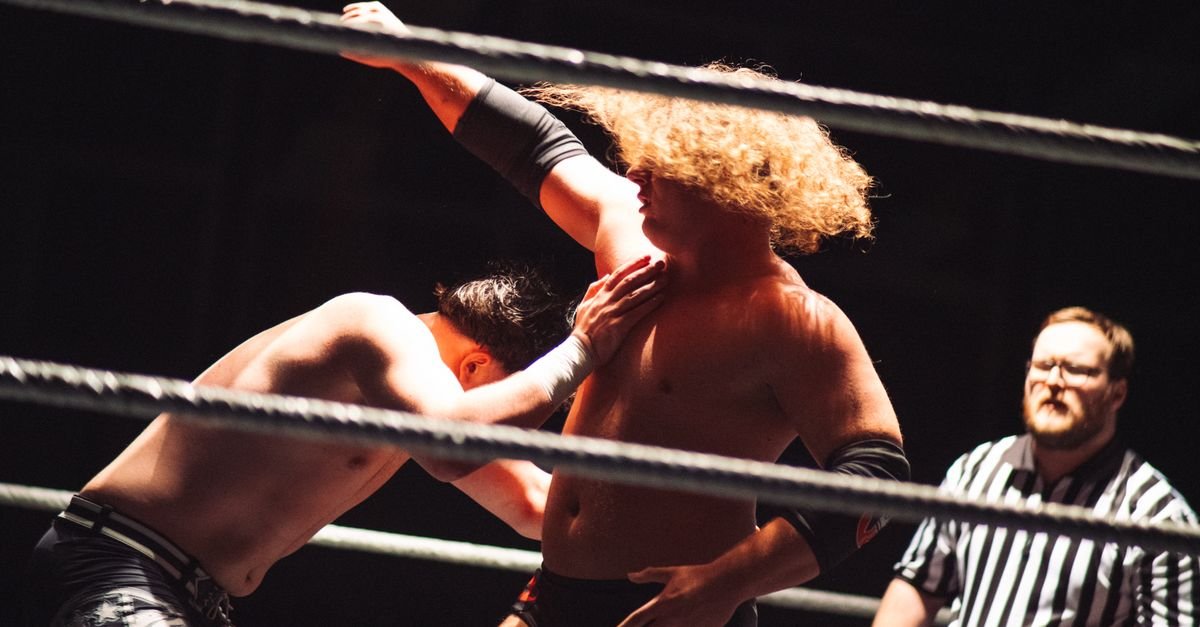 Dramatic wrestling scene with referee coaching competitors in the ring.