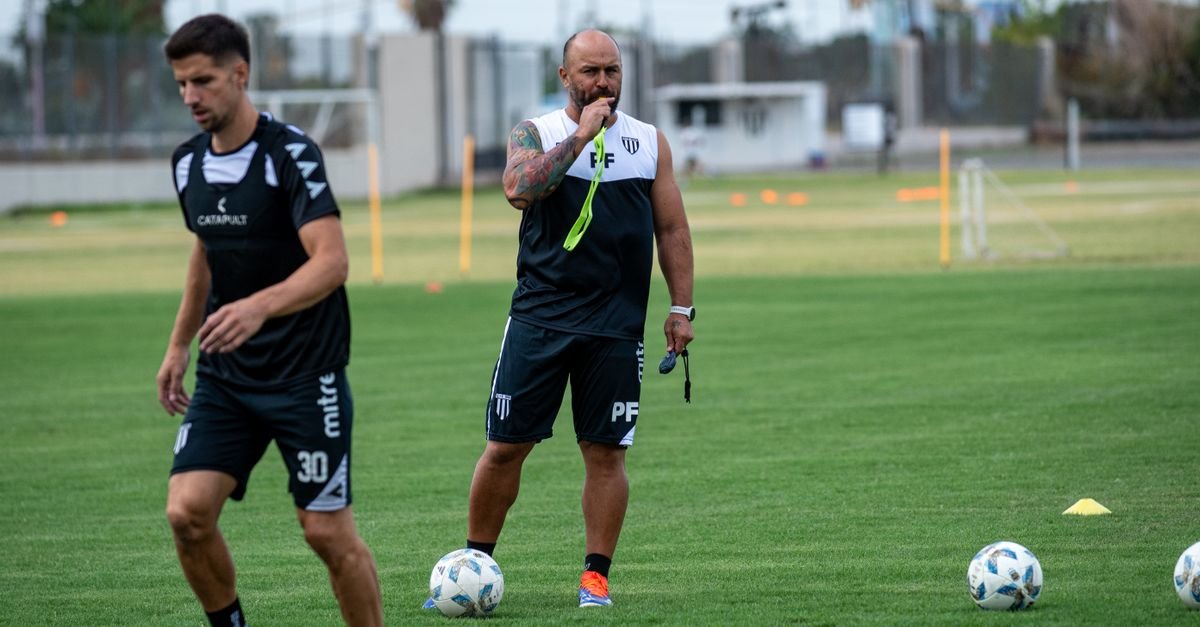 Focused soccer coach instructing players during a training session on a green field.