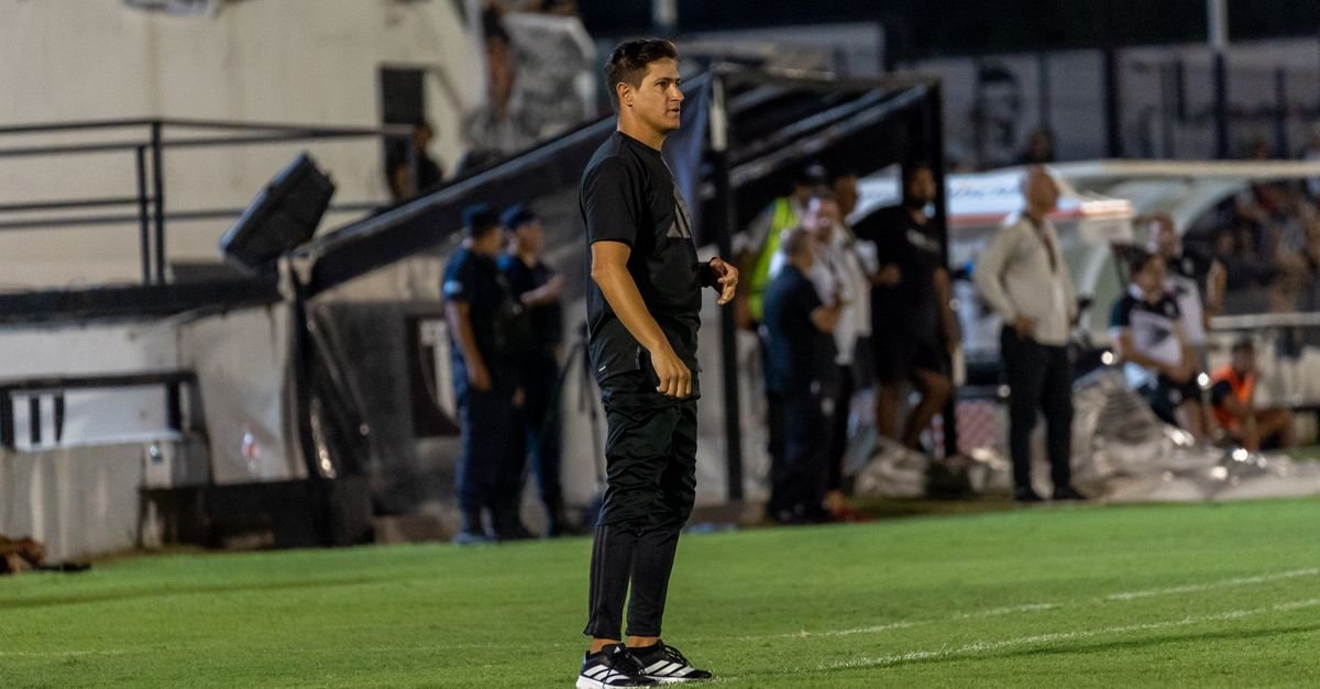 Focused football coach stands on the field sidelines during an intense match at night.