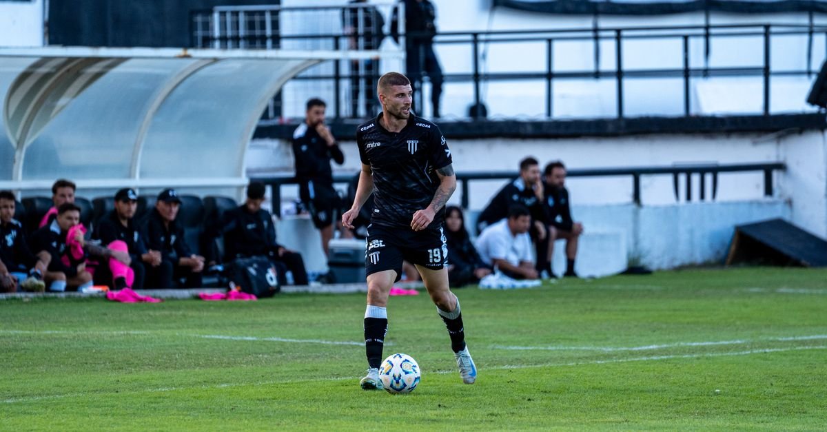 Soccer player dribbling during a match with team watching from the sidelines.