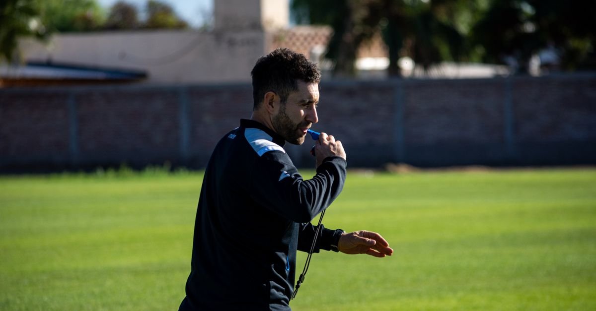 Football coach blowing a whistle during practice on a sunny day outdoors.
