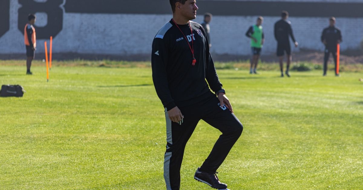 Adult soccer coach guiding players during outdoor training on a sunny day.