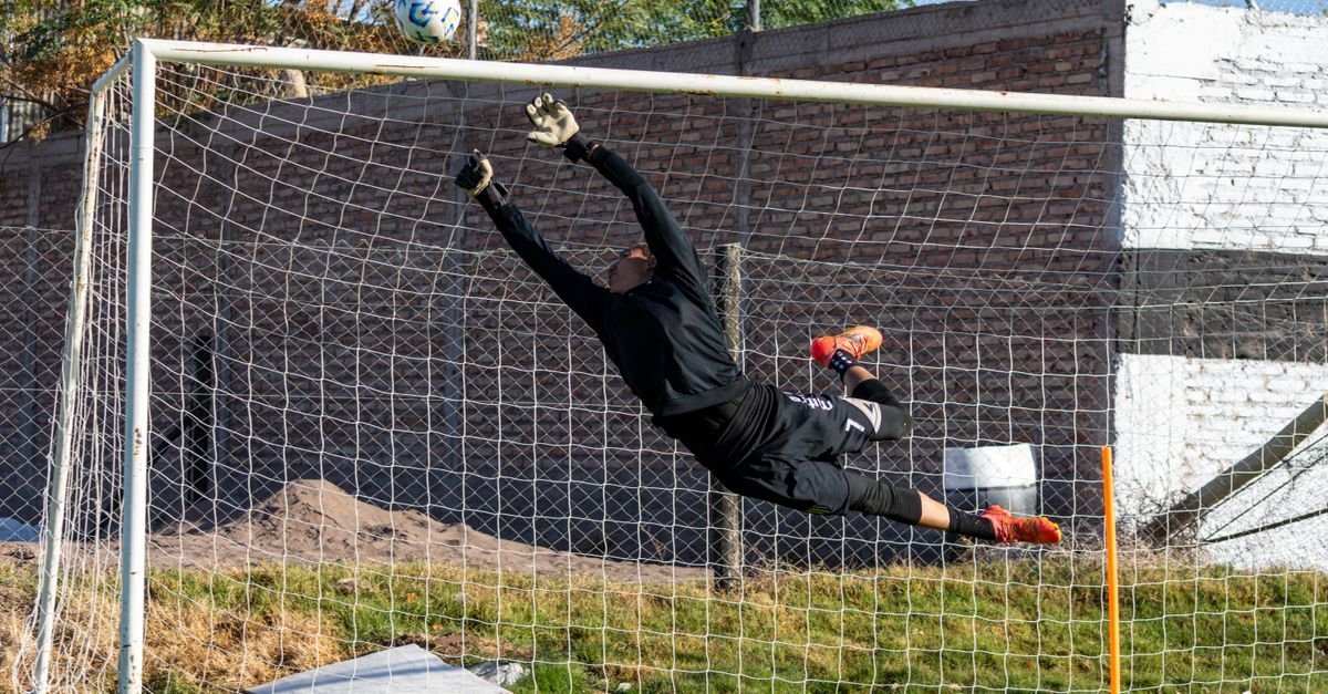 Dynamic action shot of a goalkeeper making a high save during a soccer game outdoors.