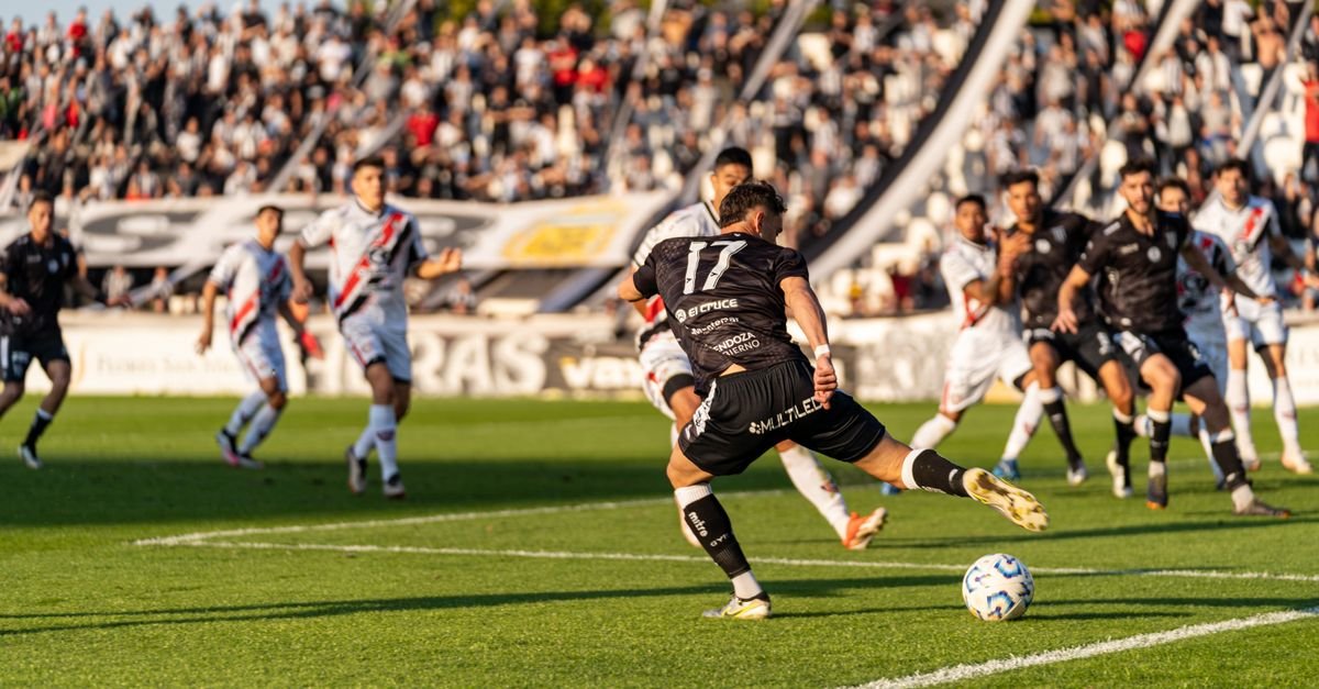 A dynamic football match with players in motion on a sunny day, witnessed by a packed stadium.