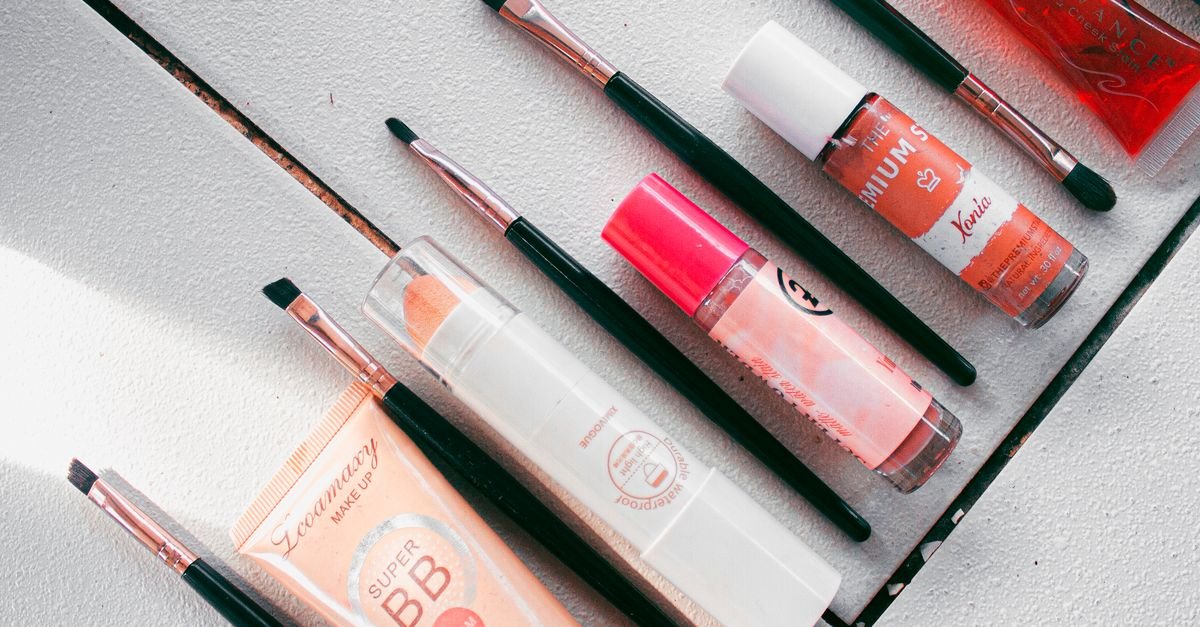 Flatlay image showcasing various makeup products and brushes arranged on a white surface, ideal for beauty themes.