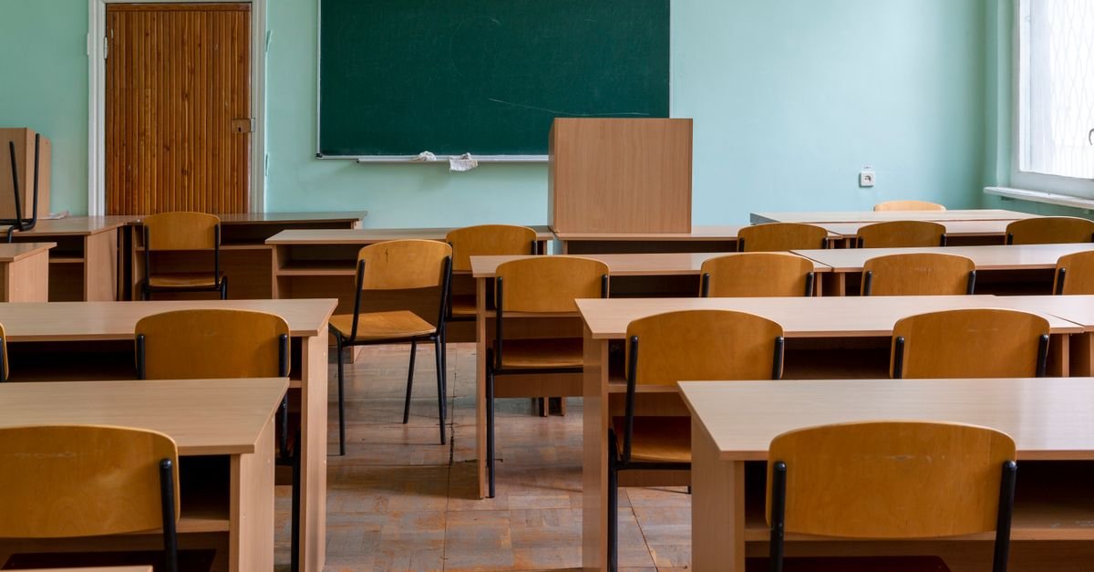 An empty classroom featuring wooden desks, chairs, and a large green chalkboard.