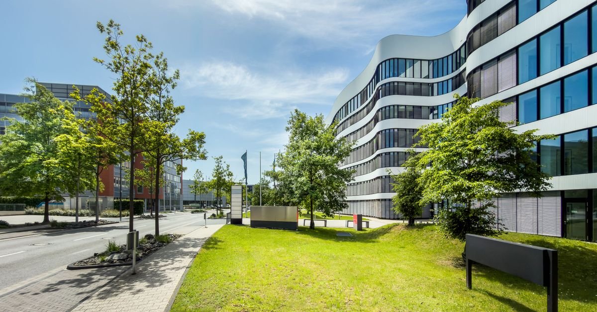 Contemporary business office building with curved architecture and trees in an urban setting.