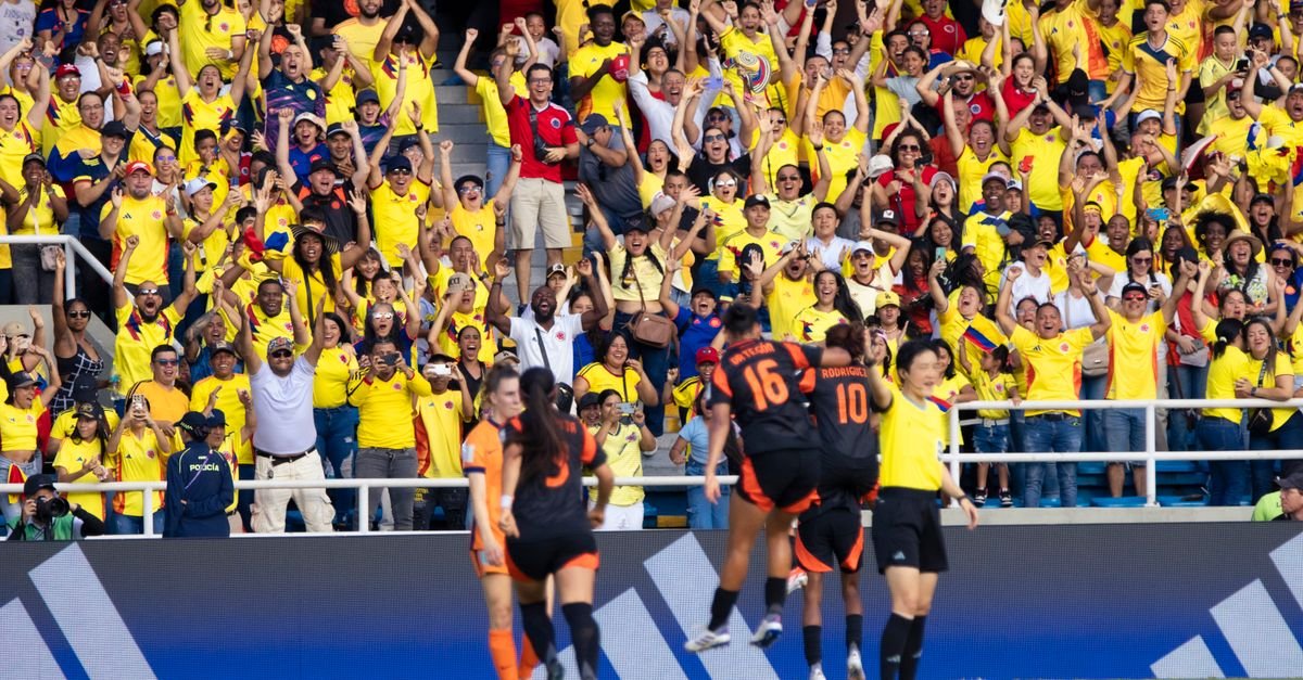 Energetic crowd of Colombian football fans cheering at a match in a vibrant stadium.