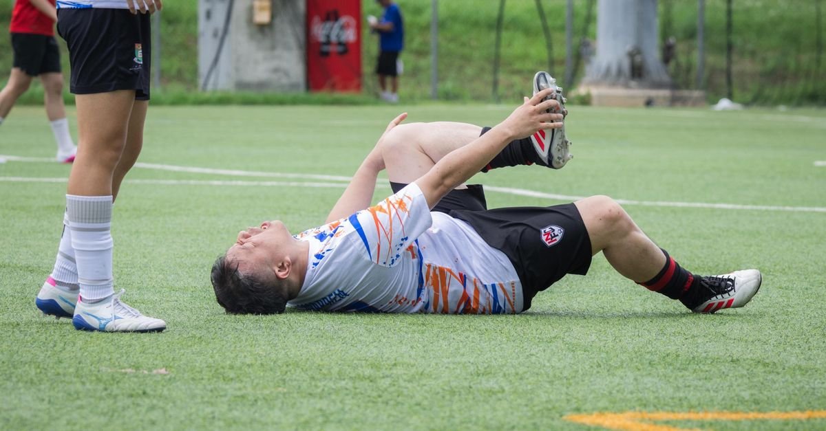 A soccer player lies on the field with an apparent leg injury during a game, needing assistance.