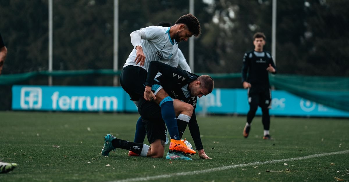 Footballers engaged in an intense match on a grassy outdoor field during the day.
