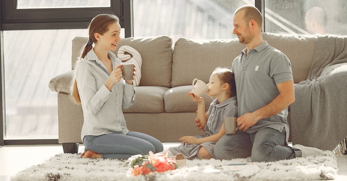 Cheerful family drinking tea in living room while having rest and laughing together during weekend while spending time and having fun