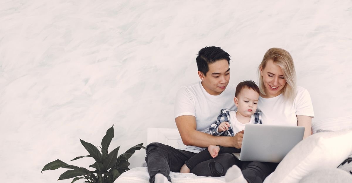 A young family enjoying quality time together using a laptop on a cozy bed.
