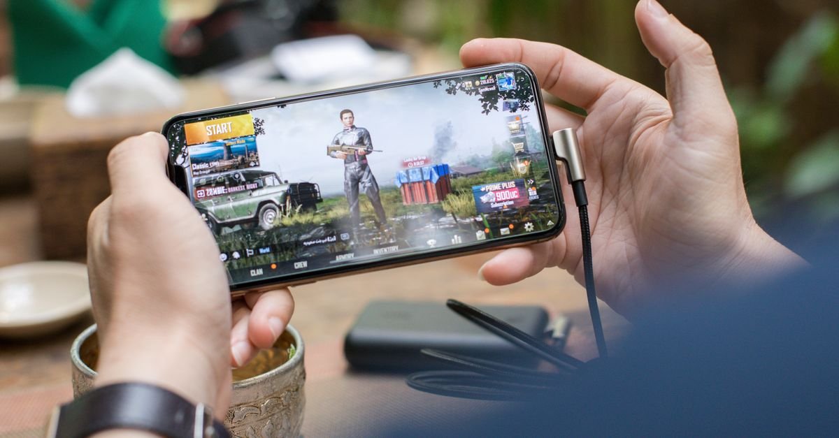 Person playing PUBG on smartphone outdoors with charging cable attached.