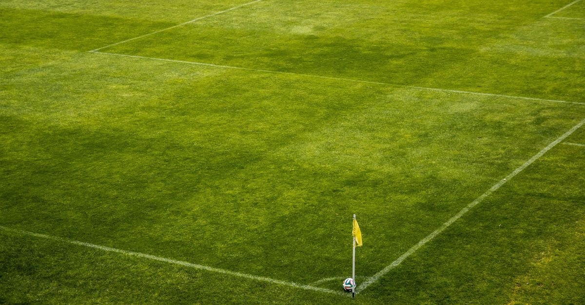 A vibrant green soccer field corner with a yellow flag and soccer ball, perfect for sports themes.
