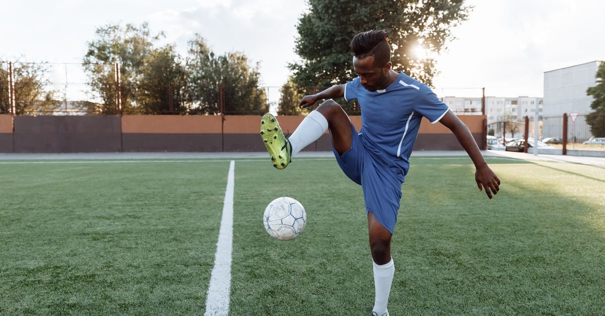 Young football player practicing tricks with a soccer ball on a sunny day outdoors.