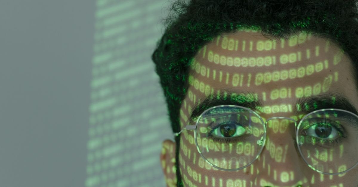 Close-up of a man with binary code projected on his face, symbolizing cybersecurity.