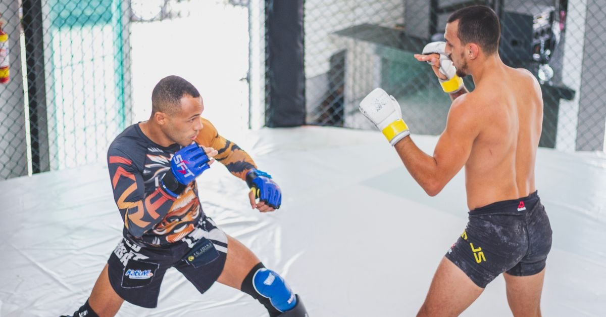 Two male fighters engaged in a mixed martial arts sparring session within a cage.