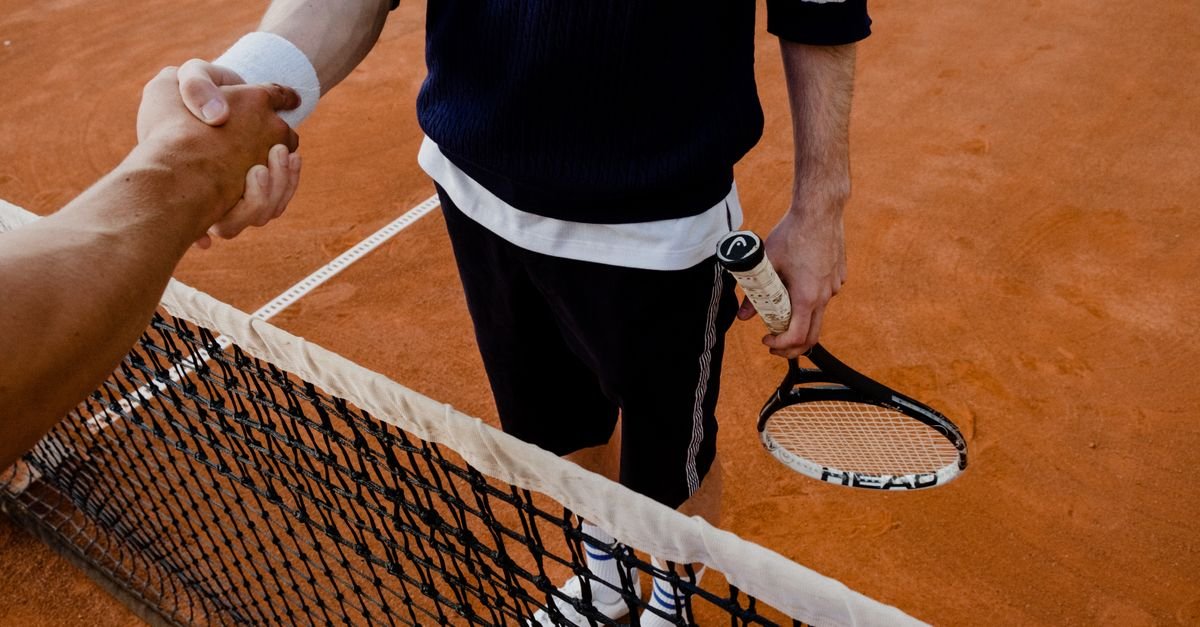 A close-up of tennis players shaking hands over the net on a clay court.