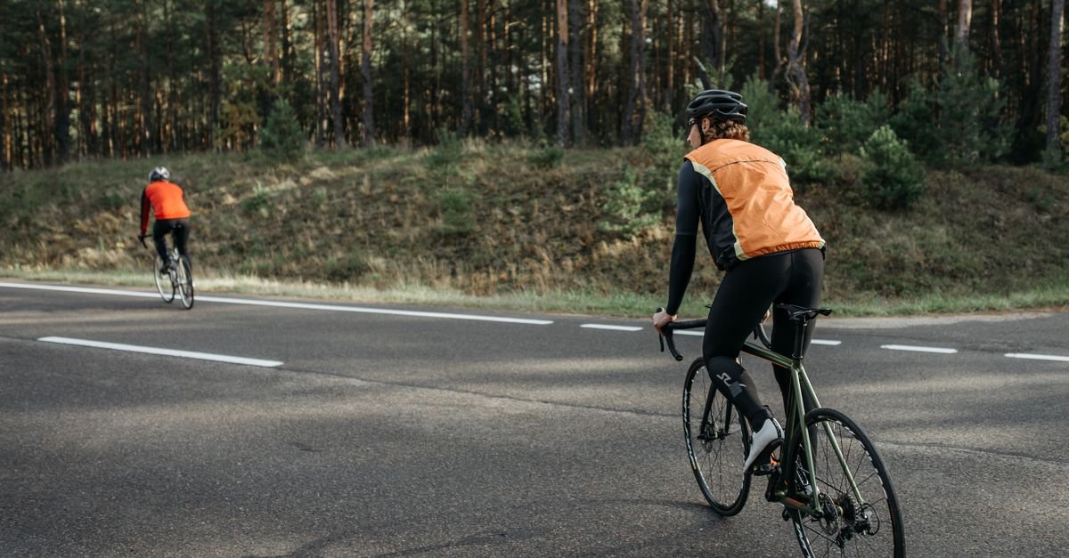 Two cyclists wearing reflective vests riding on a forest road, embracing nature and fitness.