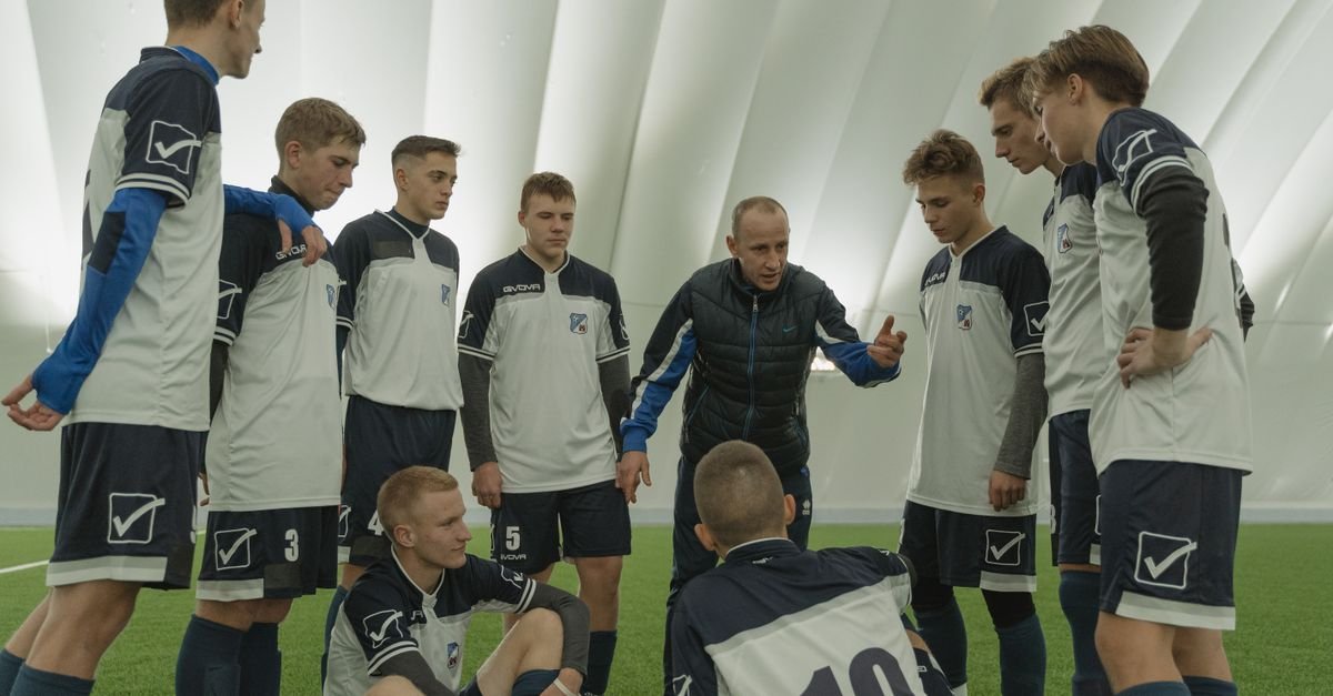 Coach giving a pep talk to a men's soccer team indoors.