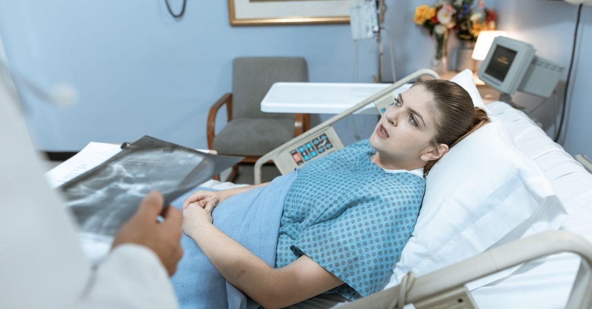 Caucasian woman in hospital bed receiving care from healthcare professional.