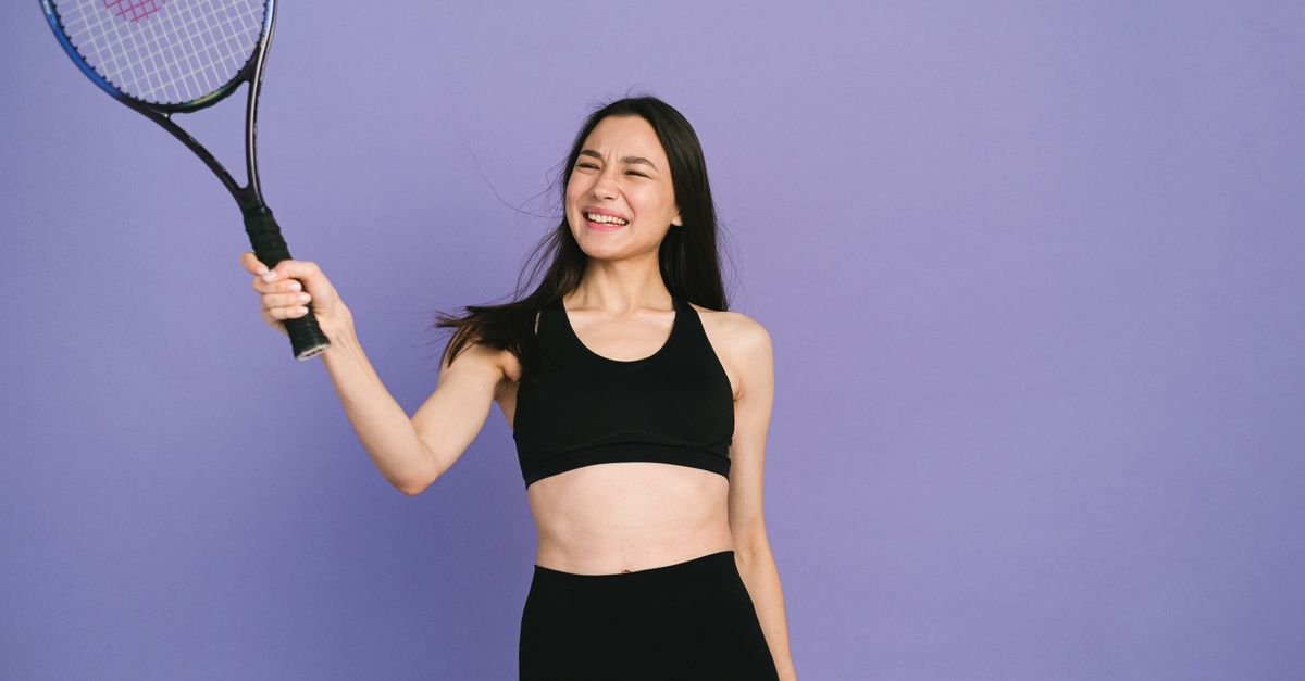Young woman in activewear holding a tennis racket, expressing joy and energy.