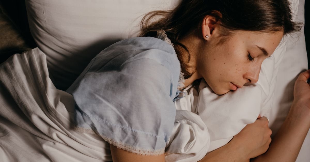 A serene young woman peacefully sleeping on a white pillow indoors at night.